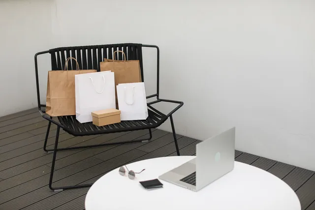 A stylish scene of online shopping with a laptop and various shopping bags on a chair. Indication des prix pour les clients de l’UE: ce que doivent respecter les e-commerçants suisses