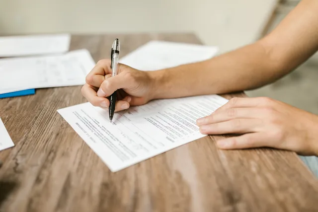 Hand filling out paperwork with a pen, showcasing focus on document completion. Spedizioni verso l'UE: dichiarazione doganale, IVA all'importazione e giustificativi